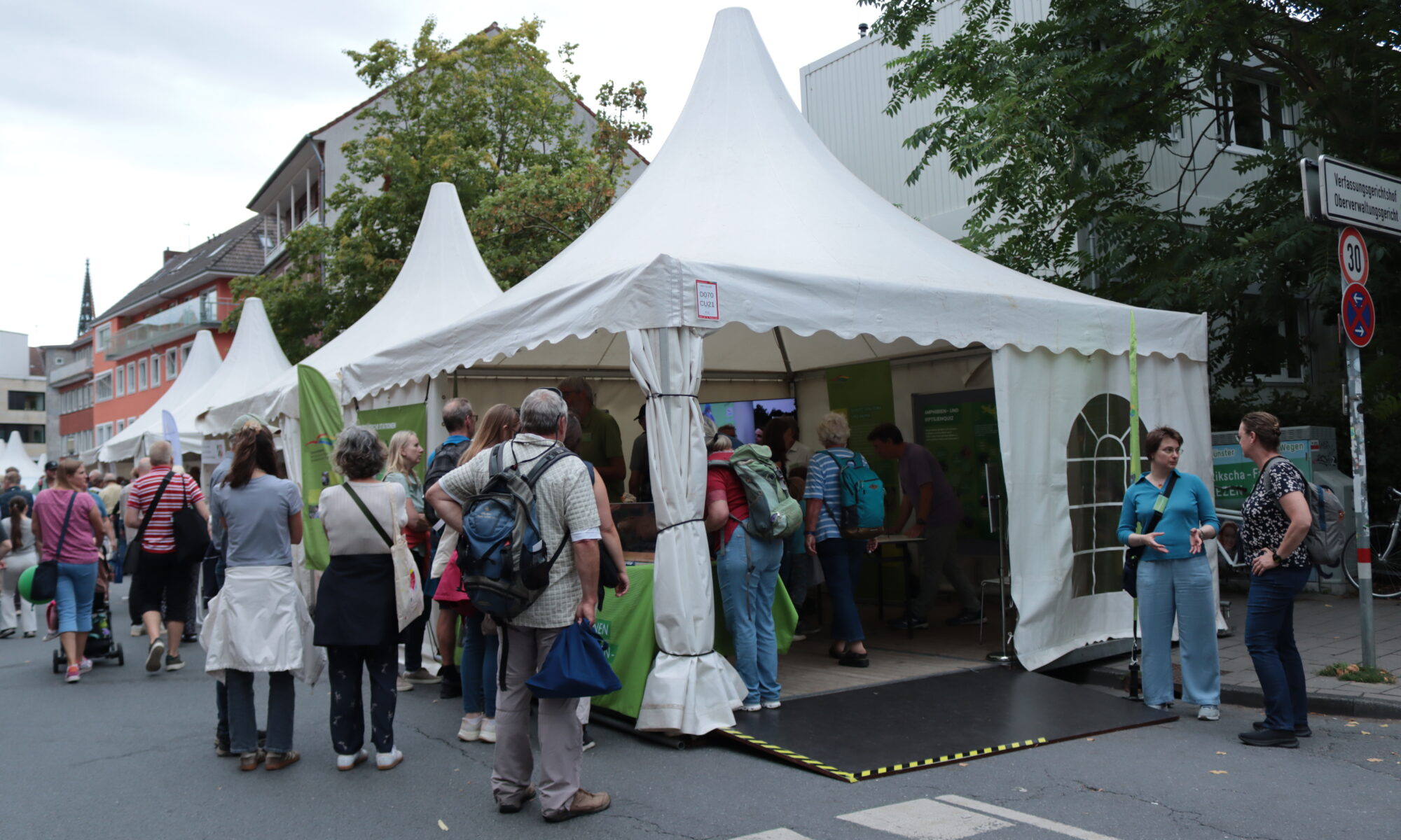 Weißes Zelt mit Ausstellungsobjekten der Biologischen Stationen und vielen Menschen.